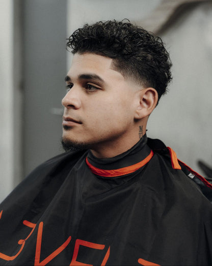 Man with styled hair wearing a black and orange barber cape in a salon setting.