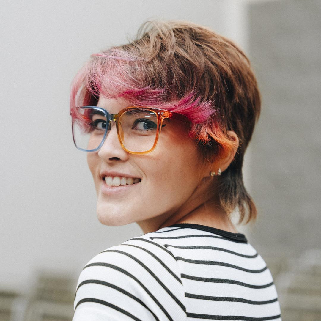 Person with short hair and colorful highlights wearing glasses and a striped shirt.